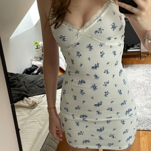 Vit blommig klänning med spetsdetaljer - Säljer denna superfina vita klänning med blå blommor och spetsdetaljer. Klänningen är tight och kort, perfekt för sommar och fest. Är i jättebra skick och i storlek XS, men är väldigt stretchig och passar mig som brukar ha S💞