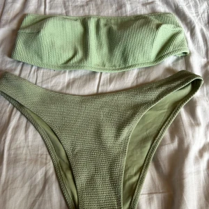 Grön ribbad bikini - Säljer en superfin grön bikini i ribbat material. Överdelen är en bandeau-stil utan axelband. Bikinin är aldrig använd och köptes förra året från H&M💗Du kan köpa toppen eller underdelen för 60kr/st eller båda för 110kr🥰