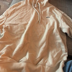 Beige hoodie med texten 'LOVE' - Säljer en supermysig beige hoodie med texten 'LOVE' på bröstet. Den är i storlek XXS och har en klassisk känguruficka framtill. Perfekt för höst och vinter när man vill hålla sig varm och bekväm. Den är i bra skick och redo för en ny ägare!
