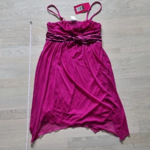 Oanvänd rosa justerbar klänning - Helt ny med prislapp på. Klänningen är fodrad och justerbar. För barn ca 150 cm (12 år). Måttband på bilderna finns som referens. Mer exakt storlek finns på lappen på klänningen på bild 3. Nypris: $29.99