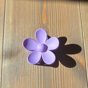 Lila blommig hårklämma - Säljer en ny superfin lila hårklämma formad som en blomma. Perfekt för att sätta upp håret på ett snyggt och enkelt sätt. Klämman är gjord av plast och har en stark fjäder som håller håret på plats hela dagen. Passar perfekt för både vardag och fest!