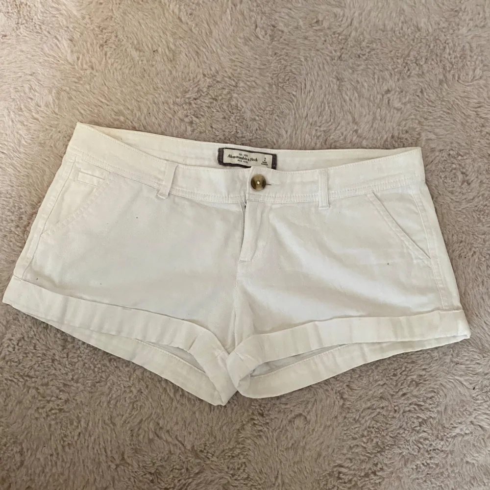 Säljer ett par vita shorts från Abercrombie & Fitch i storlek S. De är gjorda av bomull och har en knapp och dragkedja framtill. Shortsen har fickor både fram och bak, och en liten broderad logga på baksidan. Perfekta för sommaren!💕. Shorts.