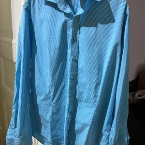 Blå/vit-randig skjorta. - Skjorta i slim fit från dressmann. Storlek M. Jättefint skick och inga skavanker. Två extra knappar medföljes. 