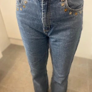 Blåa Jeans  - Jeans med broderade blommor vid farm fickorna. Storlek 38