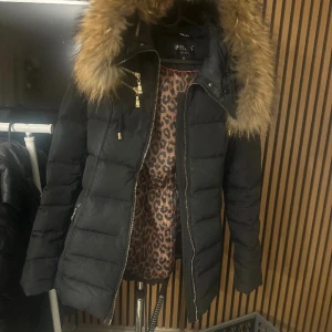 Holliesjacka  - Svart, figursydd dunjacka i kortare modell från Hollies. Luva med avtagbar pälskrage, storlek 40.  I jättefin skick. 