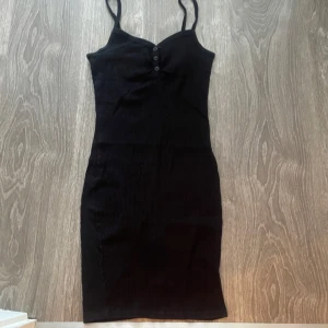 Klänning - ribbad, svart, kort, tajt, har knappar på framsidan, funkar för både Xs och S.   Kontakta för mer info/fler bilder. Kan postas men köpare står för frakten. Kan mötas upp i malmö. 