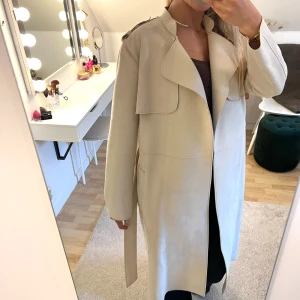 Beige kappa i mocka - Så snygg beige kappa/trenchcoat i mocka med fickor och ett band att knyta runt midjan 💓 Nyskick, storlek S. Är 167 cm lång och normal S/M.