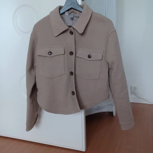 Skjortjacka - En supersnygg jacka i en kortare modell. Snygg beige färg o fina detaljer. Välsydd .  HELT NY!