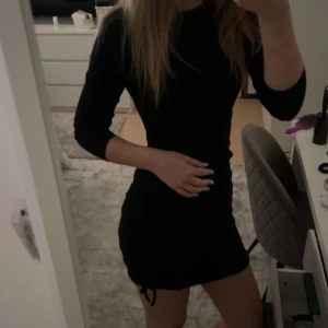svart klänning  - Klänningen är långärmad men ärmarna har blivit för korta för mig därför har jag dragit upp dom lite. Ribbat material(se bild 3). Aldrig använd, nyskick. Den har snörning på sidan. Den är i 152 men skulle säga att den passar xxs.Skriv för fler frågor!