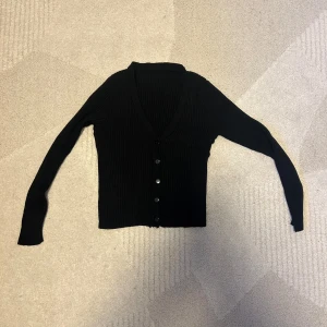 Svart kofta med knappar  - Säljer denna svarta ribbade koftan i storlek XS och använts ett par gånger. Koftan är fortfarande i fint skick. 
