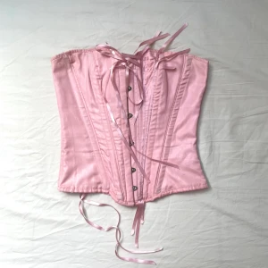 Vintage rosa korsett - Rosa vintage korsett med fina detaljer. Har tyvärr lite fläckar/tecken på användning, se bilder. För övrigt i gott skick. Justerbar i storlek beroende på hur tight den knyts. 