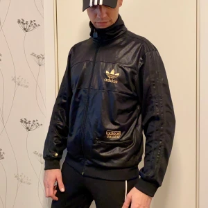 Adidas Chile 62 trackie jacka stl M - Cool svart glansig Adidas jacka, väl använd men fortfarande mycket att ge. Se bilder för skick.