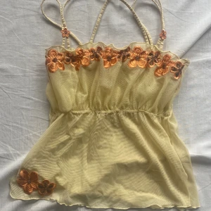 Blommig pastell topp - Söt topp i färgen gul med blommiga brodyr detaljer. Obs toppen är genomskinlig