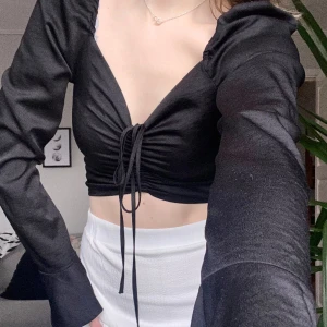 Svart topp - En svart fest topp med lite vidare ärmar från BikBok! Knytdetalj fram som går att justera. Fint skick, storlek xs