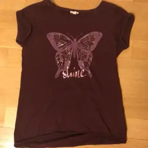 T shirt från Sprit! Lila/vinröd. En lila fjäril på framsidan med texten ”Shine”. Hör av dig om du undrar något 💜
