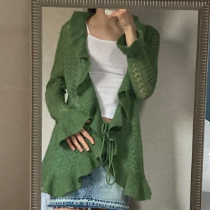 Grön kofta med volanger  - Jätte fin grön stickad lång kofta med volanger och utsvänga volang ärmar, snören till för att stänga koftan🤍 Passar så fint till en minikjol🌟 Nyttskick! Säljer då jag köpte en annan🫶🏼 Passar mig som har storlek S men passar även M.