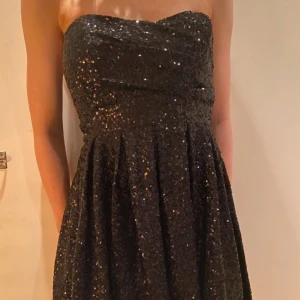 Svart glittrig klänning  - Jättefin off-shoulder klänning, glittrig med svarta paljetter.  Passar S-L den är väldigt stretchig. Har gummi längs kanten så att den inte åker ned.  Använd 1 gång på temafest, känner inte att jag kommer använda den igen. 