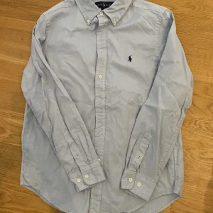 Ralph Lauren skjorta - Säljer en nästan oanvänd ljusblå Ralph Lauren skjorta, storlek 18, barn.  Var några år sen jag hade på mig den, men skulle tro den passar runt 160-170.