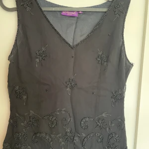 Festlinne med paljetter - Svart festlinne med mönster av pärlor och paljetter. Storlek S. Märke Diwali. Blixtlås i sidan. 