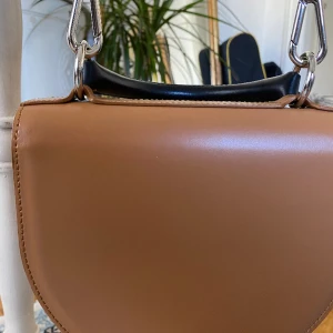 Marimekko brun läderväska/ crossbody - Marimekko crossbody väska i äkta läder. Aldrig använt och köpt för cirka 2800 kr. Går att hämta i Majorna, centrum eller fraktas mot avgift. Inga fläckar eller defekter. Metalldetaljer i silver.  Höjd 20 cm. Bredd 17 cm, djup 7,5 cm.