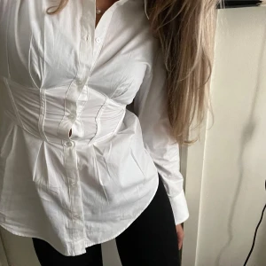 Milkmaid bomullsskjorta - Säljer min vita korsettskjorta från H&M då den blivit för liten för mig. I nyskick!! Använd 2-3ggr. Lappen är avklippt med passar en strl 34 (XS/S). Smock i ryggen. 🤍 Mått (cm): Längd: 62, midjevidd: 70-80, armhåla-armhåla: 90.