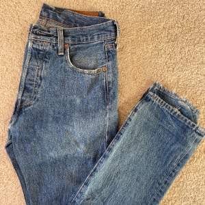 En par Levis 501 jeans i en lite urtvättad mörkblå färg. Jeansen har slitna defekter längst ner men utöver de kan man säga att skicket är utmärkt. 