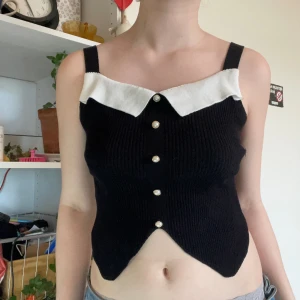 Svart topp med vit krage - Känns lite sjömansaktig med små pärlknappar och en vit krage. I ribbat tyg. Märke okänt men tyget är ett bra och stretchigt material, endast använd ett fåtal gånger. Storlek anges inte, ungefär S.