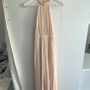 Väldigt fin balklänning från Nelly - Fin långklänning perfekt till bal/bankett. Använd 1 gång, puderrosa, fint tyg med slits på ena sidan. Halterneckmodell med fina detaljer och öppen rygg. Nelly eve collectionen 