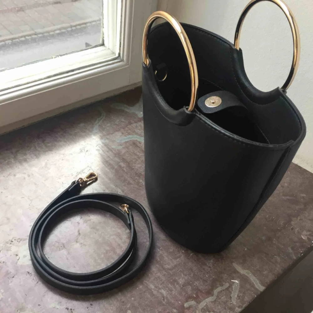 Så söt svart bucket väska med guldringar, axelremmen kan knäppas på eller av. Använd en gång så den är i nyskick! Ca 23cm hög.   Möts i Malmö!. Väskor.