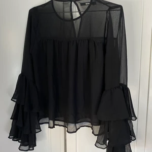 Blus med volangärmar - Svart, genomskinlig blus med volangärmar som tyvärr inte kommer till användning längre. Sparsamt använd, så i gott skick! Strl. S. Säljer för 100 kr exkl. frakt som tillkommer :) Har även nyckelhålsöppning i ryggen!