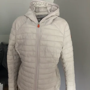 Save the duck ultra light jacket - Köpt för ca 2000 och den är knappt använd. Den är i storlek 2 som är medium enligt deras storleks guide. Superfin beige vit färg som ser ännu finare ut i verkligheten. Jackan är i vattenavvisande material.