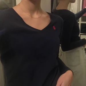 Ralph Lauren tröja - En superfin marinblå t-tröja från Ralph Lauren som blivit för liten för mig. Den ser fräsch ut, men har blivit solblekt på ena armen och har två små hål på framsidan, hålen syns knappt men blekningen på armen är ganska tydlig. Fint v-ringad! 