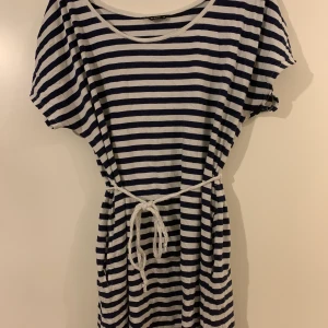 Vit/blå randig klänning - 38 - Vit blå randig klänning i storlek 38 men fickor precis under bandet i midjan. 50kr+ frakt. 