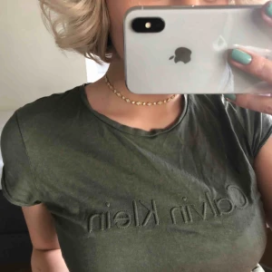  - Camouflage grön T-shirt från Calvin Klein jeans. Sitter tjat. ”Bra att ha” vardagsplagg, man sträcker sig enkelt efter den när det är bråttom. Gillar att styla med stora ringar. 