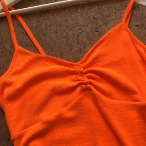  - Tight, ribbad neonorange klänning med veck på bysten. Superskön, mjuk, stretchig. Endast använd en gång. Tyvärr har det uppstått lite små noppor efter en dålig väska jag hade, se tredje bilden. Frakt tillkommer!