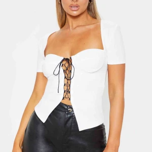 Vit topp med snörning - Vit topp med snörning från Prettylittlething. Aldrig använd då kuporna var för små. Storlek 10 (38), men är som en 34/36. 