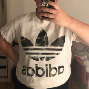  - Vit adidas tröja med militär tryck. Fösta bilen är t-shirten instoppad.