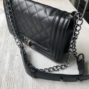 Svart väska med kedjeband - En snygg praktisk väska som är perfekt för en utekväll eller till vardag. Den är lite sliten vid spännet men annars i mycket bra skick! Priset är inklusive frakt!