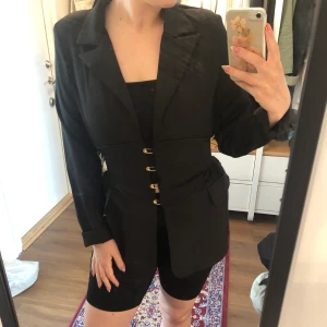 Skjortklänning - Svart skjortklänning med korsettliknande passform med knappar i guld. Helt oanvänd och frakt ingår i priset. 