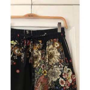 Blommiga byxor från Zara - Ett par supersköna och luftiga byxor från Zara i storlek XS. Högmidjade, vida långa ben och gummiband samt snörning i midjan. Använd Max 2 ggr