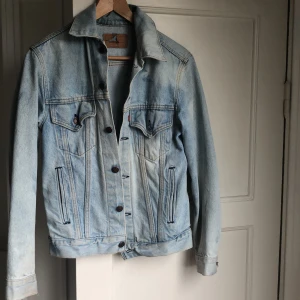 Levis jeansjacka  - En blå jeansjacka från Levis. Den är köpt vintage för 600kr. Jag tror den skulle blekas och har blivit olika nyanser blått, vilket ger jackan dess charm. säljer pågrund av lite användning och tkr inte den bara ska hängas på galgen:)