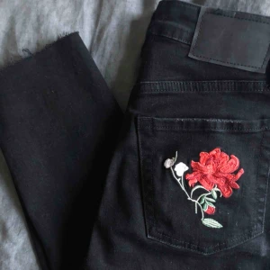  - Svarta jeans från H&M i storlek 36. Knappt använda. Fina broderade röda och rosa blommor fram, vid ankeln och på bakfickan. Slitningar nere vid fötterna. Sitter jätte fint!! Frakt ingår💞