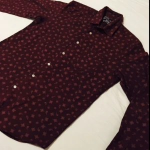  - Mörk/vinröd mjukt och lite grövre tyg med paisley liknande detaljer/mönster på. Helt oanvänd och som ny. Passformen är inte slim utan mer standard. 