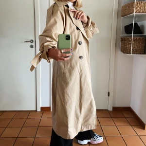 Beige kappa/trenchcoat  - Beige kappa/trenchcoat från Lindex, sitter snyggt oversized på mig som normalt sätt har S i jackor och är 170. På 1:a bilden är bältet knytet i ryggen. Köpt på second hand men med orginallappen på då och nästan aldrig använd av mig, så i fint skick! Köparen står för frakt☺️