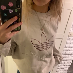 Adidas collagetröja - Snygg adidaströja i ljusbeige med vinröd/lila logga i storlek 36 men skulle säga att den är något oversize för att endast ha storlek S