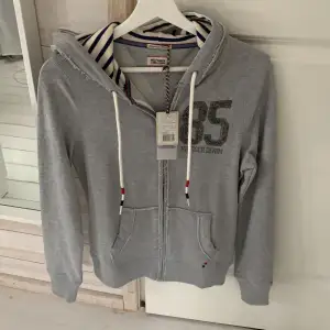 Helt ny båtimiterad Tommy hilfiger kofta. Marinblå och vit randig i luvan och två snörningar som är vita med rött och marinblått i ändarna. Ordinarie pris 1100, köpt för 770. XS passar folk mellan 170-180