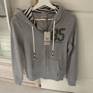 Tommy hilfiger kofta - Helt ny båtimiterad Tommy hilfiger kofta. Marinblå och vit randig i luvan och två snörningar som är vita med rött och marinblått i ändarna. Ordinarie pris 1100, köpt för 770. XS passar folk mellan 170-180