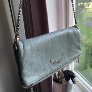 Zadig väska  - Grå väska från zadig, hel och ren i fint skick. Långt samt kort axelband medföljer. Även dustbag och kvitto! Obs, på bilden i mitten ser väska mörkare ut än vad den egentligen är, bild 1 & 3 visar mer hur färgen ser ut i verkligheten. 