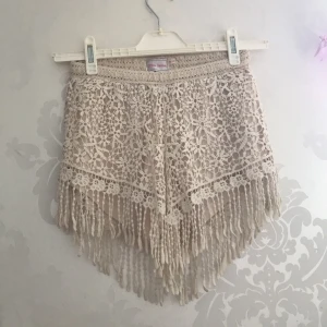 Shorts  - Söta beige shorts med blommig mönster och tofsar ner till, i storlek S. Perfekt till en promenad på stranden 🏖💖