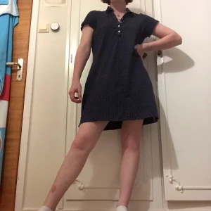 Pikétröja i blått med vita prickar - En pikétröja i XL som passar som en klänning i S. Den är mörkblå med små vita prickar. Knappar på bröstet.